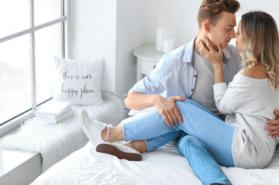 Free Image of Affectionate couple sitting on the bed in a brightly lit bedroom. 