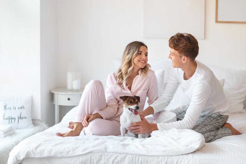 Free Image of Couple sitting on bed with their dog enjoying a playful morning 