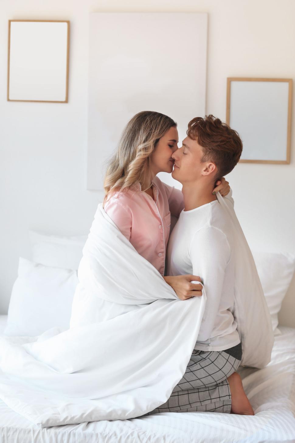 Free Image of Couple wrapped in blanket having a loving moment on the bed. 