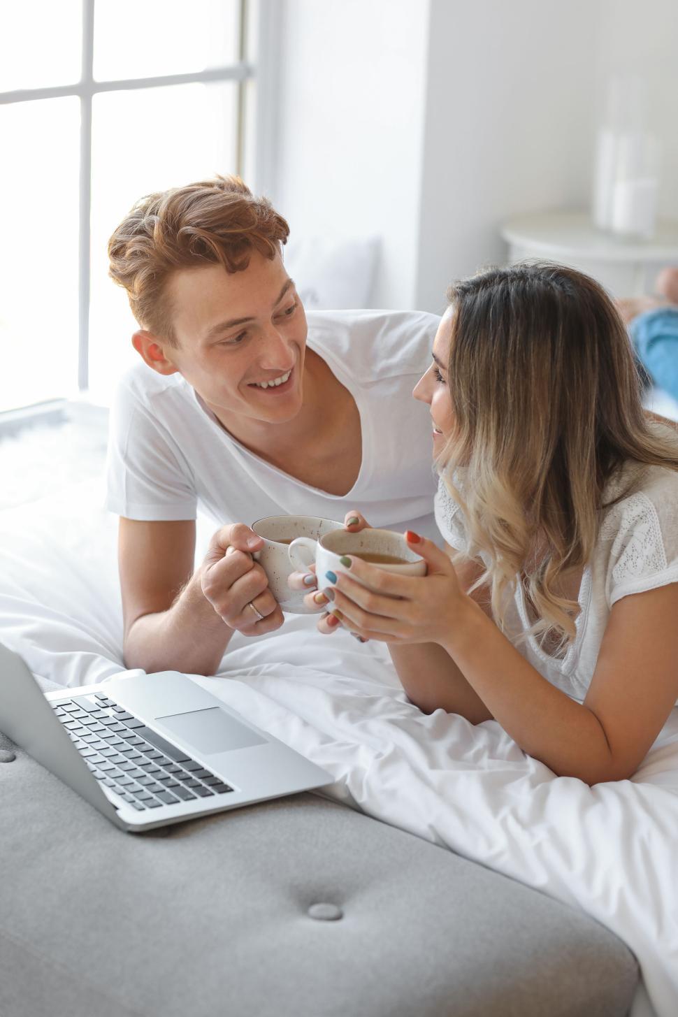 Free Image of Couple enjoying morning coffee on bed while smiling at each other 