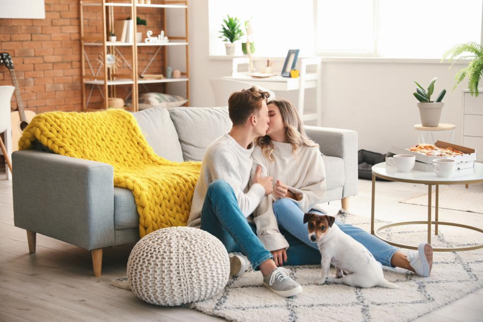 Free Image of Couple kissing on floor, dog by their side, cozy living room setting 