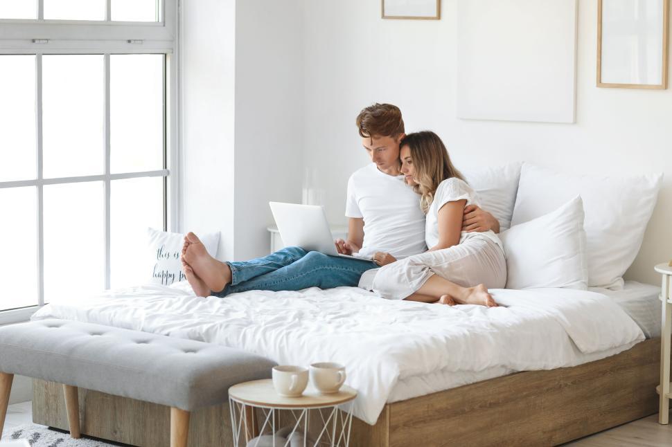 Free Image of A couple relax on bed with a laptop, nearby two cups of coffee. 