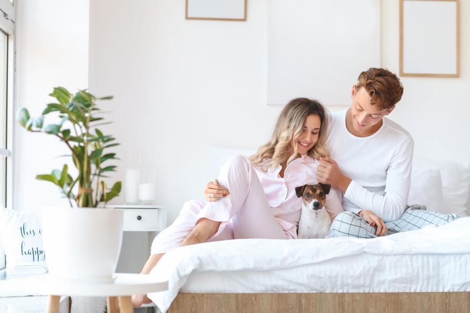 Free Image of Couple in pajamas with dog on the bed, enjoying a morning cuddle. 