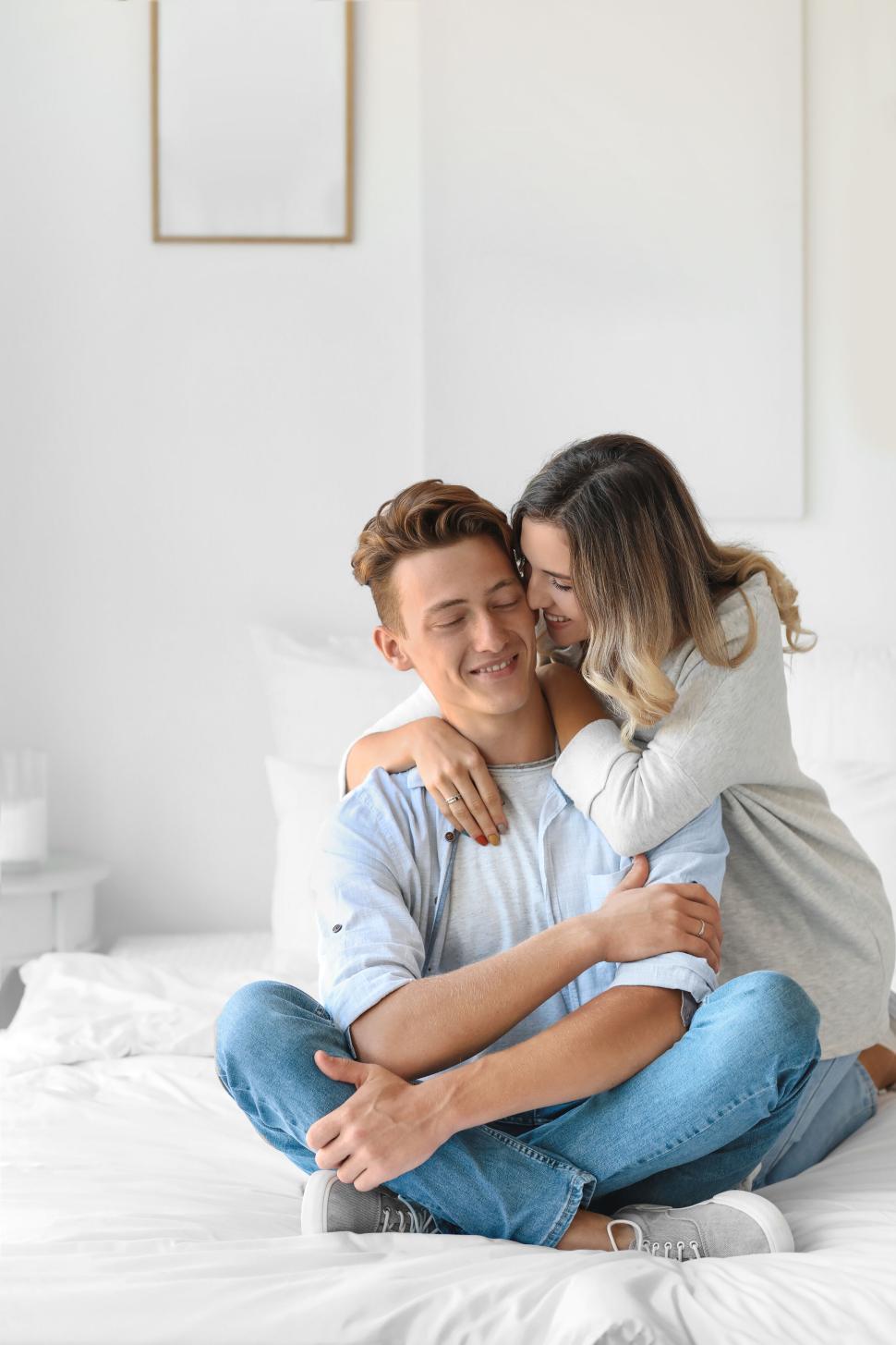 Free Image of Couple in casual attire share a hug on the bed, genuine smiles. 