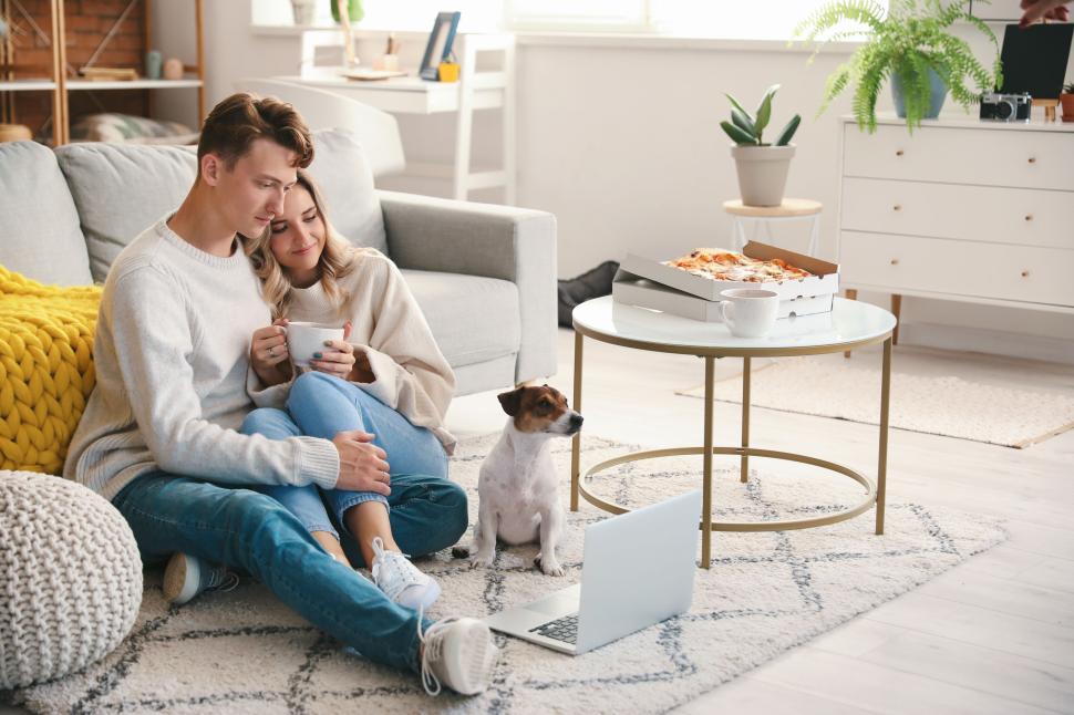 Free Image of Couple and dog in living room with pizza and laptop, casual day. 