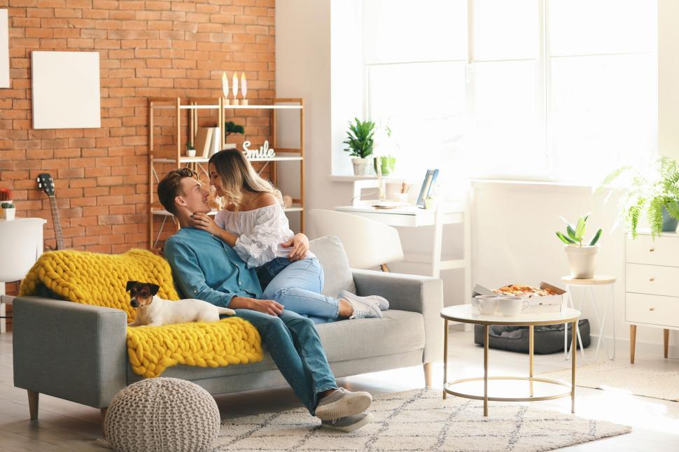 Free Image of Couple cuddles on couch with dog, enjoying a cozy, sunny living room 
