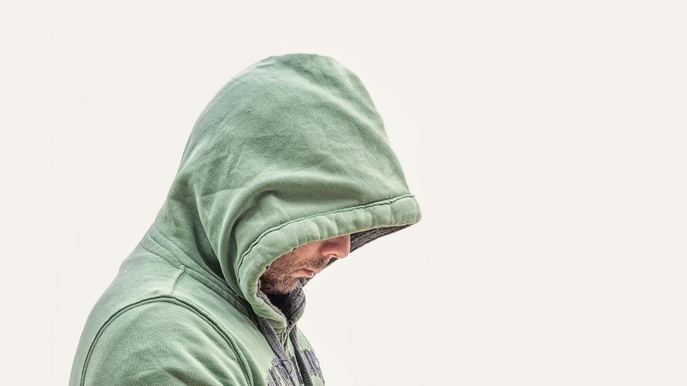 Free Image of Person in green hoodie looking down in contemplation against white 