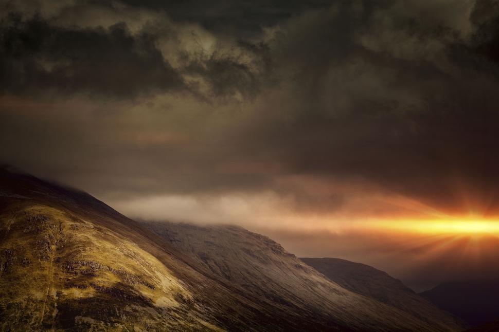 Free Image of Sunset beams over mountains, casting shadows with ominous clouds 