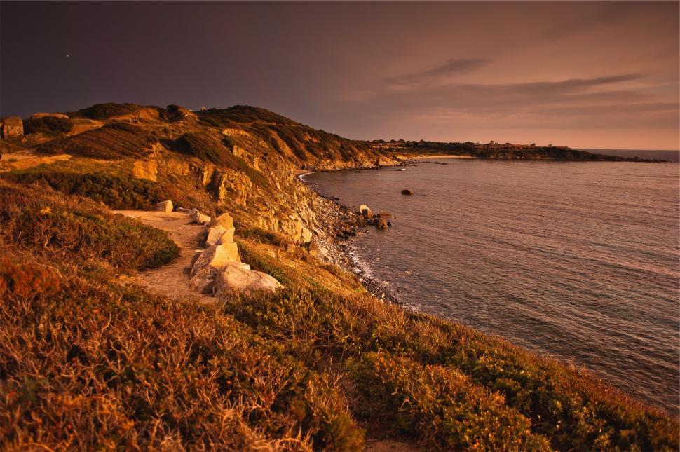 Free Image of Rocky coast at sunset with lush greenery and calm ocean waters. 