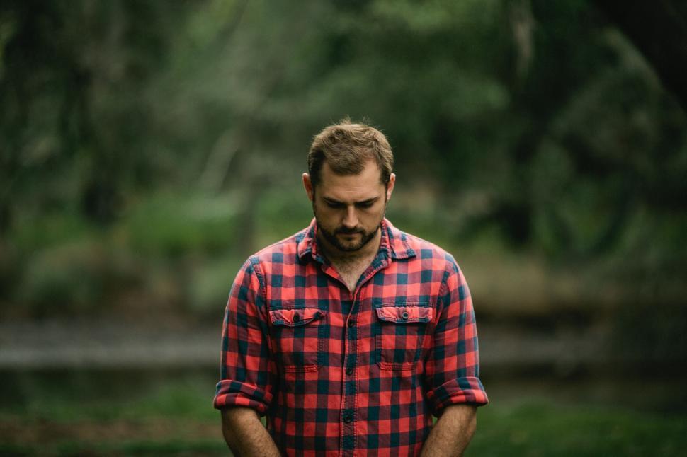 Free Image of Man in checkered shirt looking down in forest background portrait 