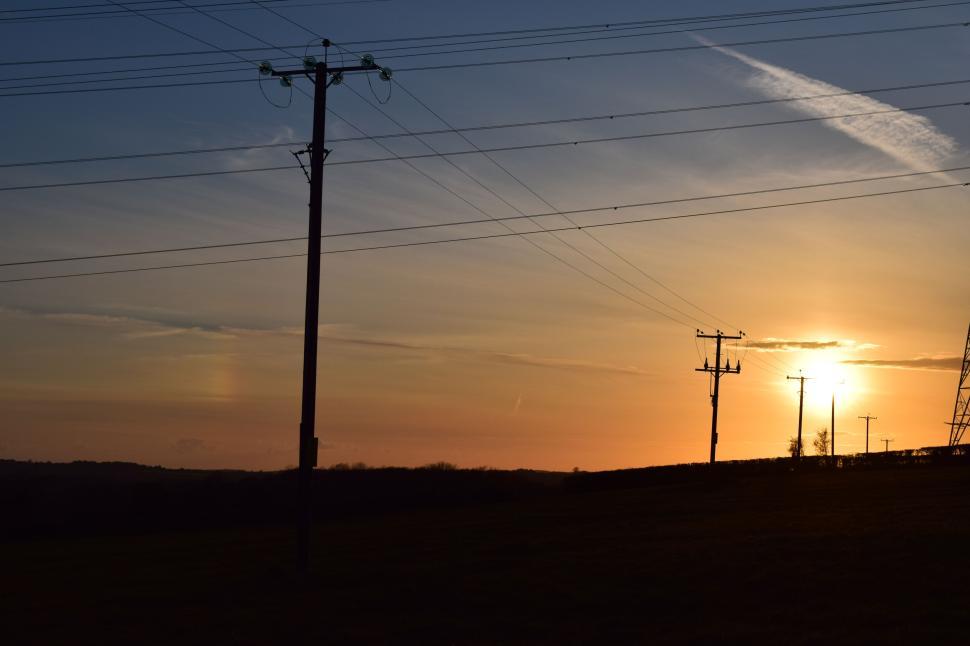 Free Image of Sunset over rural landscape with power lines and scattered trees. 