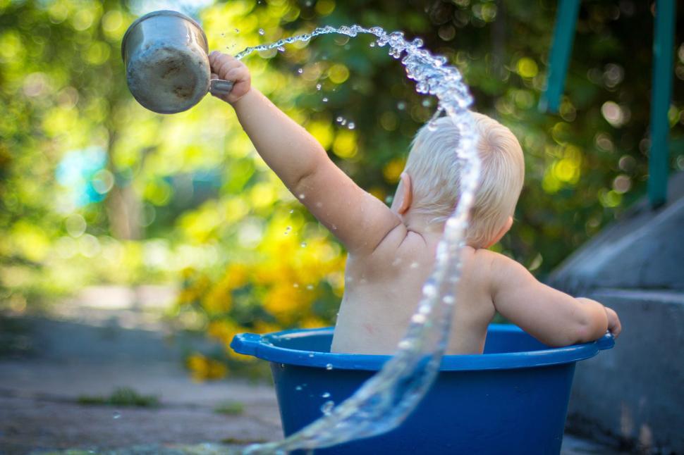Free Image of Small child playing with water in a bucket outdoors during summertime. 