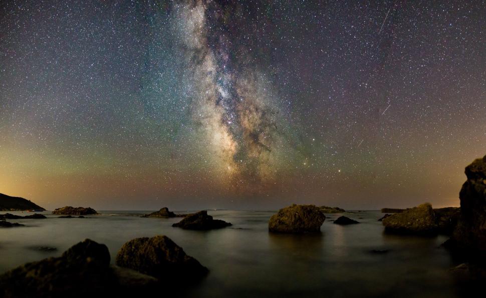 Free Image of Milky Way stretches across a stunning night sky over a rocky coast. 