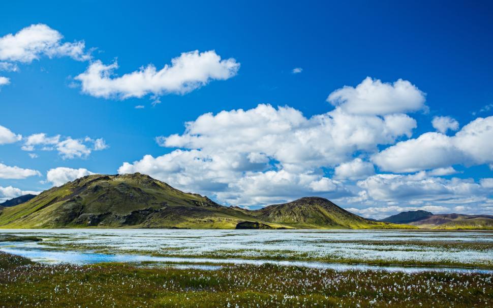 Free Image of Lush green landscape under a vibrant blue sky with scattered clouds. 