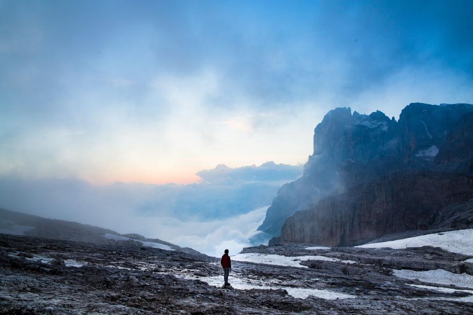 Free Image of Figure stands on rocky terrain surrounded by misty mountains at dusk. 