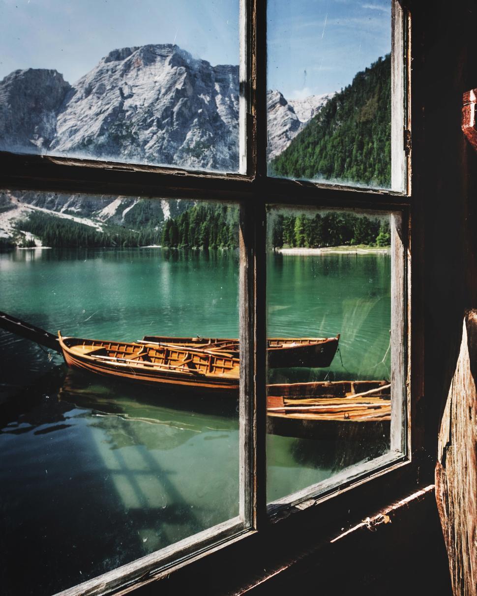 Free Image of Old wooden boats docked on a serene, mountain lake viewed from window. 