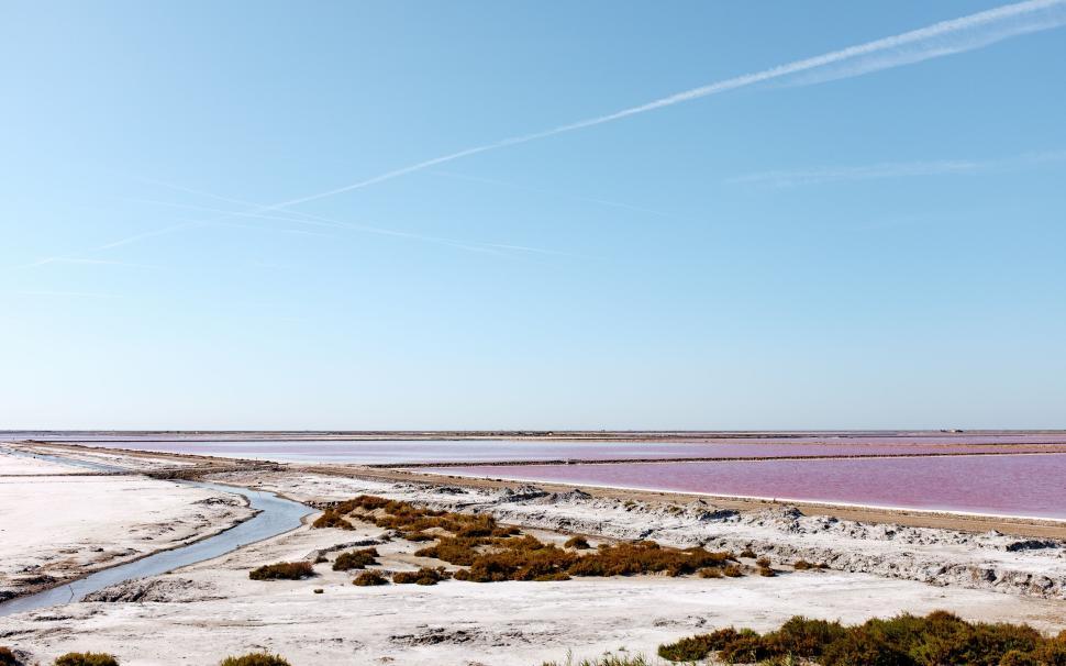 Free Image of Scenic view of pink salt flats and shallow water under clear blue sky 