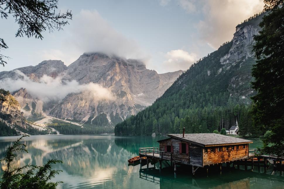 Free Image of Serene mountain lake with a cabin and mist-covered peaks view. 