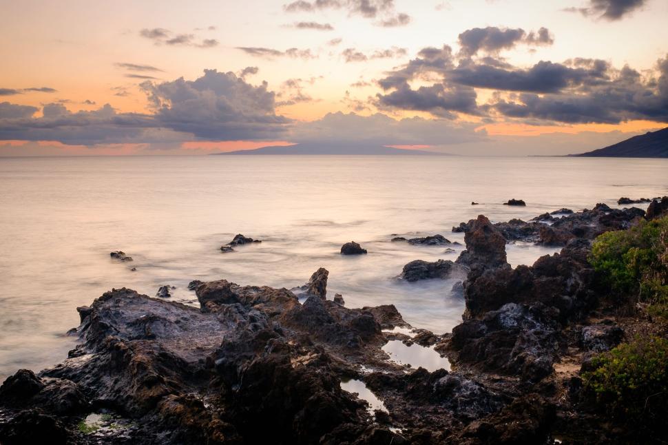 Free Image of Twilight over rocky seaside with calm waters and clouded sky 