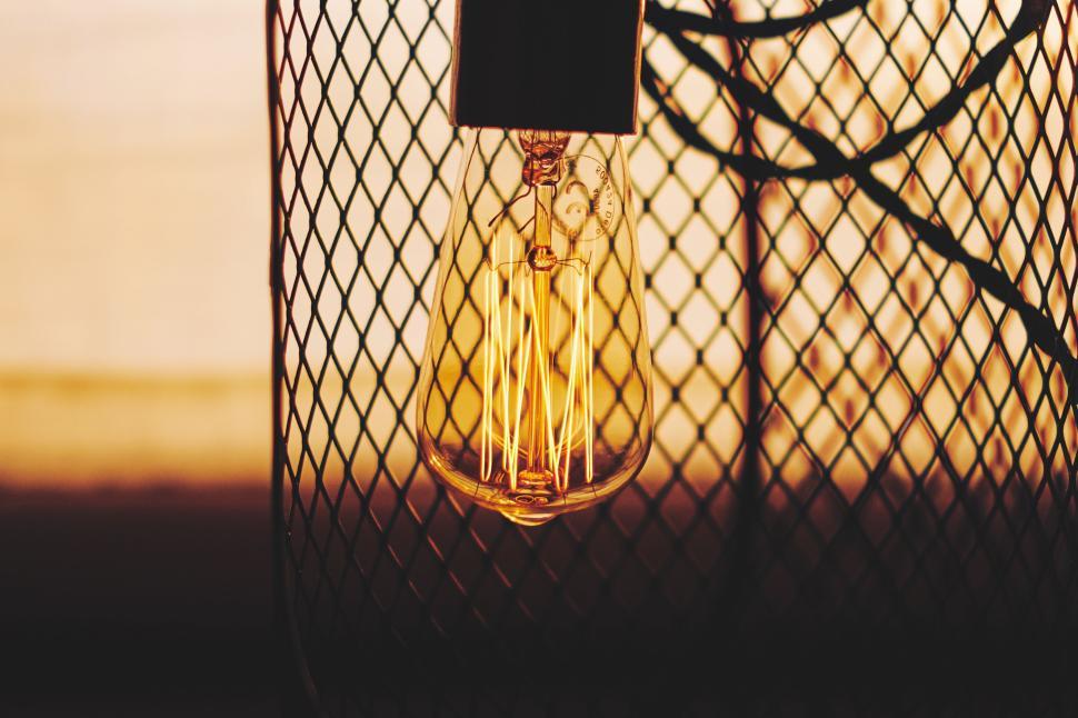 Free Image of Vintage filament lightbulb encased in metal mesh with warm glow 