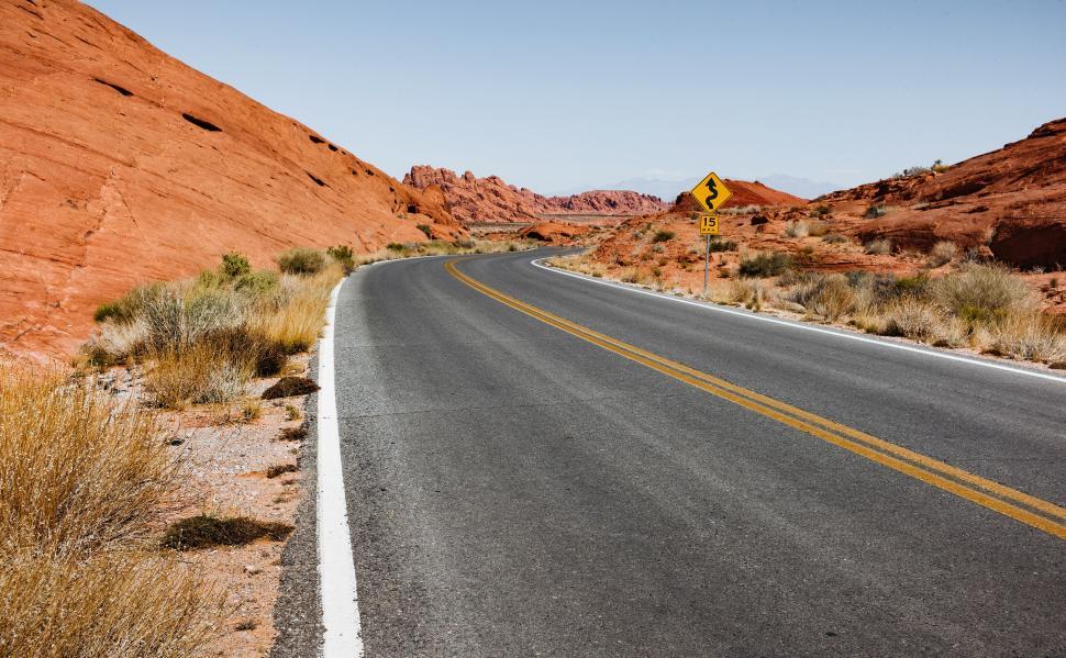 Free Image of Curving road winding through red rocky desert landscape under clear sky 