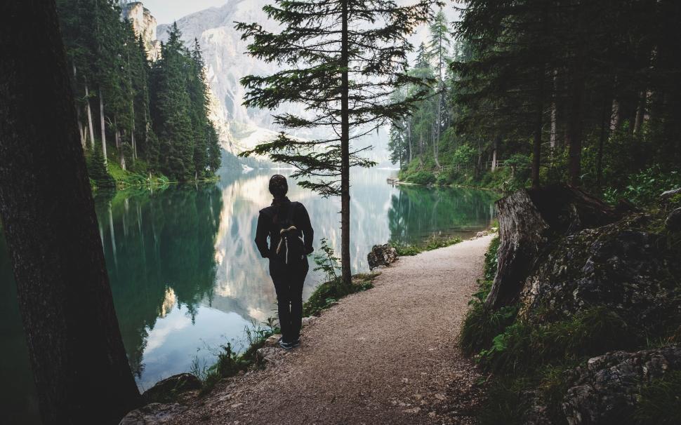 Free Image of Person with backpack walking by lakeside forest path under mountains 