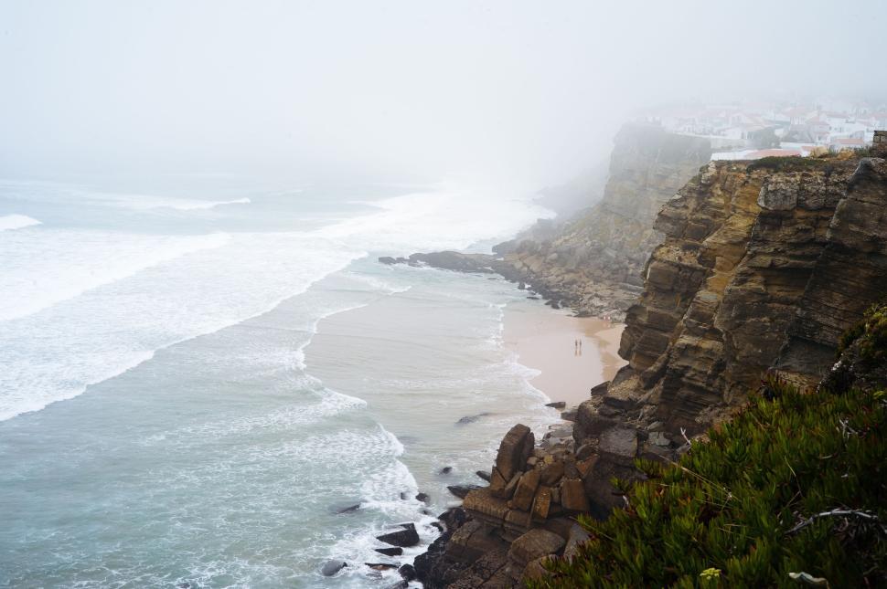 Free Image of Foggy coastline with rocky cliffs and waves crashing on the shore 
