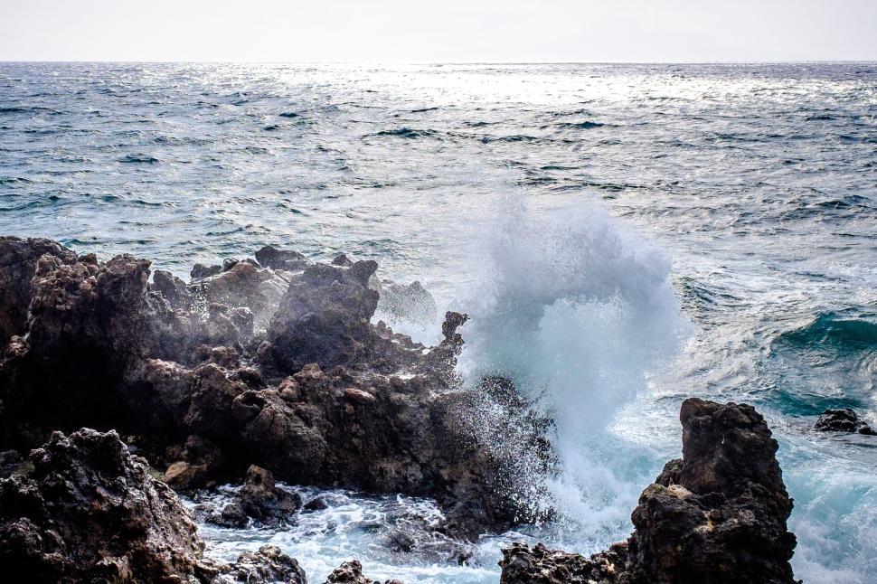 Free Image of Waves crashing against rocky shore on a bright, clear day. 