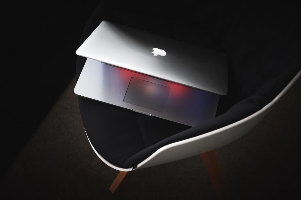 Free Image of Closed laptop with a glowing Apple logo on a modern chair 