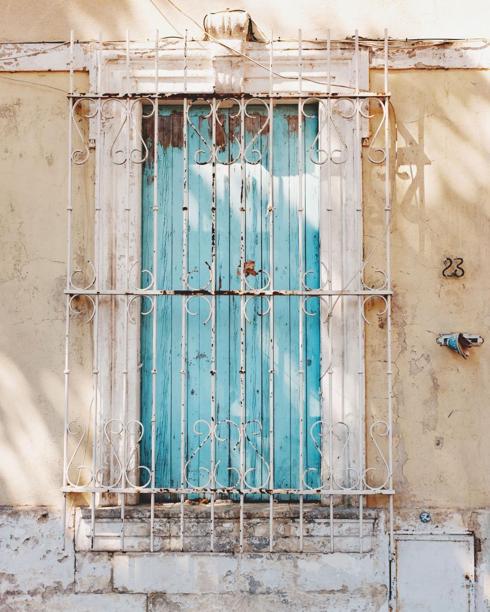 Free Image of Old blue door with white iron grate in a weathered wall numbered 23. 