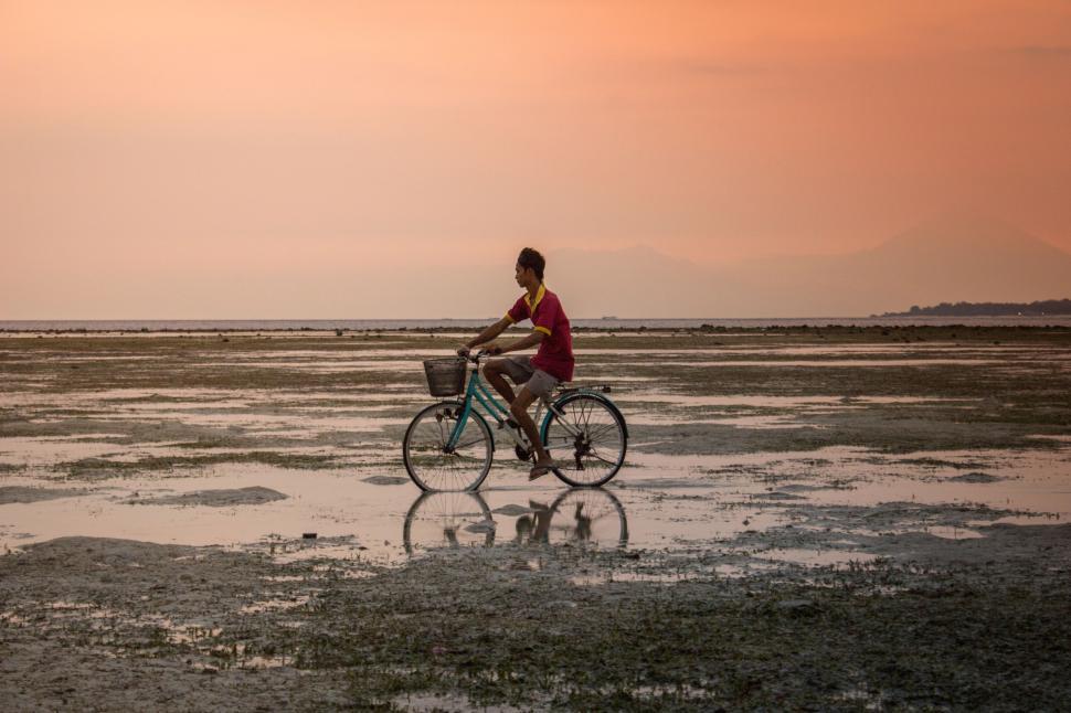 Free Image of Man riding bicycle across wet sandy terrain during sunset 