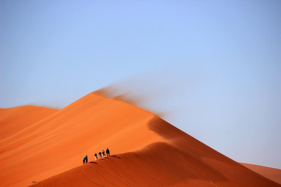 Free Image of Group of people hiking on sand dune under clear morning sky 