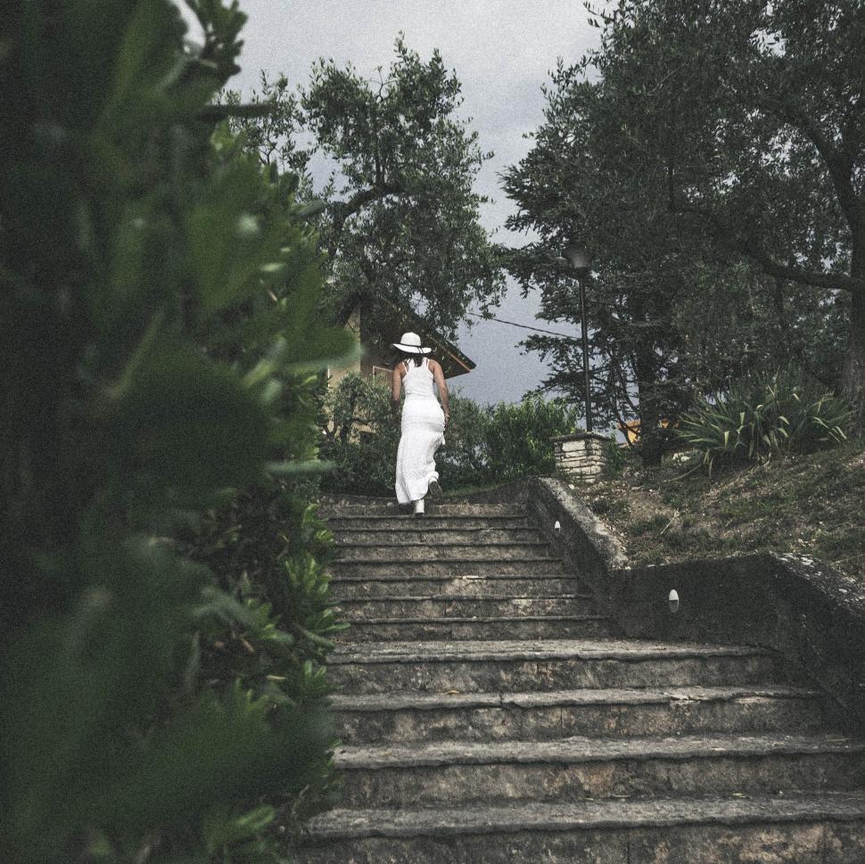 Free Image of Person in white dress and hat walking up stone garden steps 