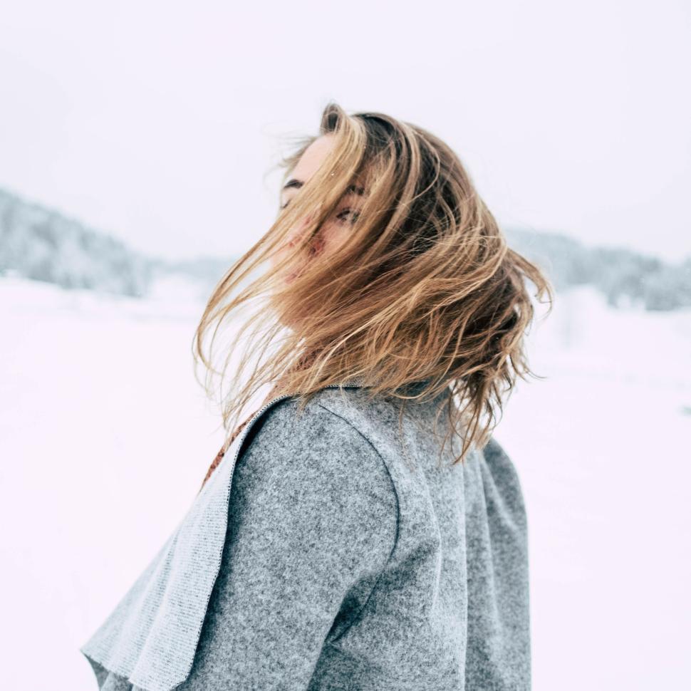 Free Image of Young woman standing outdoors in winter with snow-covered hills. 