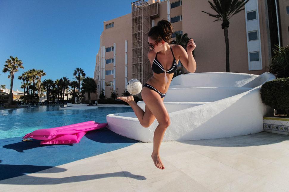 Free Image of Woman jumping near pool in swimsuit with bright sunny backdrop. 