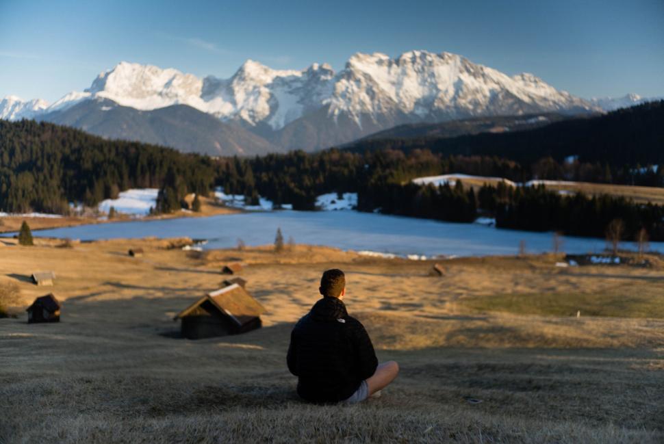 Free Image of Person meditating on a field with snow-capped mountains in background. 