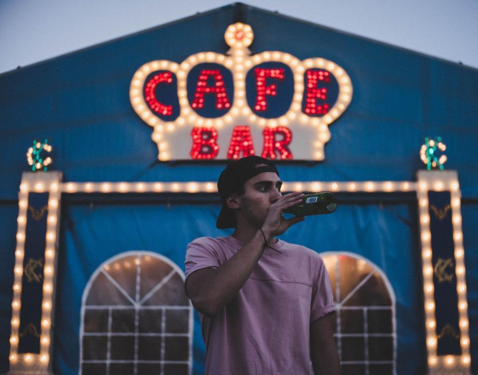 Free Image of Person sipping drink at night in front of cafe bar light display 