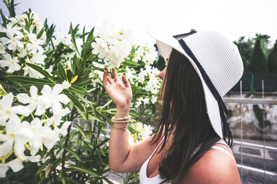 Free Image of Woman in a hat admires white flowers in a garden setting 