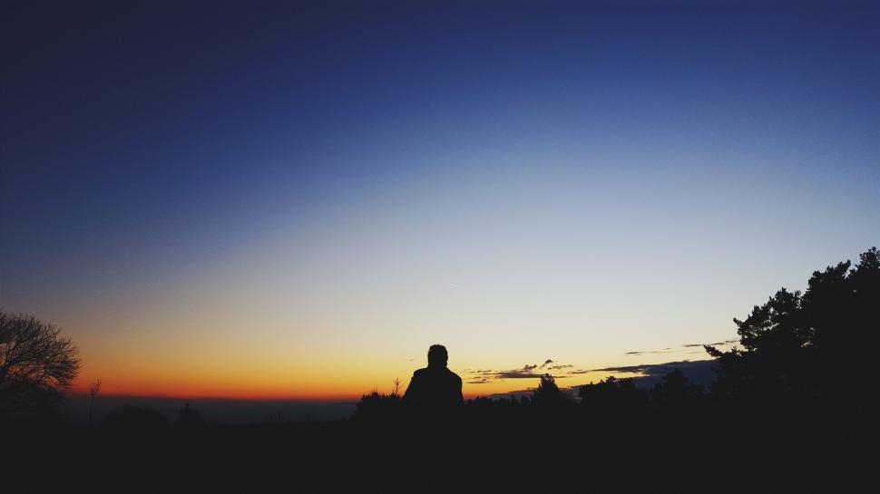 Free Image of Silhouette of a person against a vibrant sunset over a landscape. 