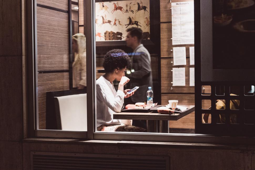 Free Image of A young woman dining alone in a fast-food restaurant at night 