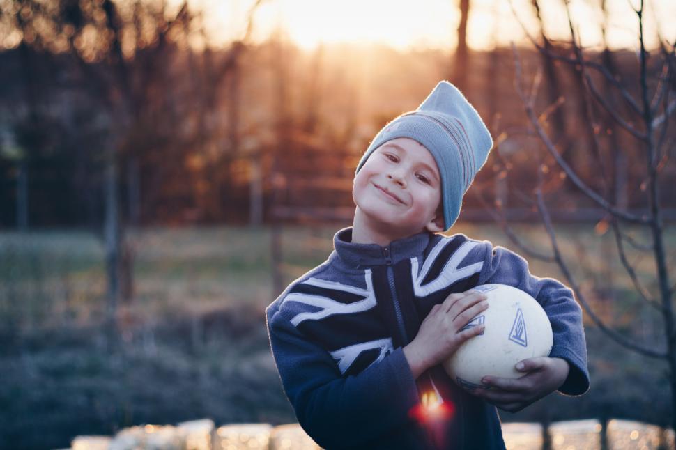 Free Image of A young child holding a soccer ball in the field during sunset 