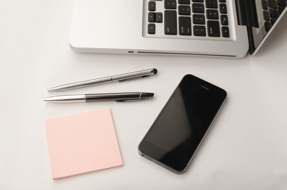 Free Image of Laptop with pens, phone, and sticky note on a light background. 