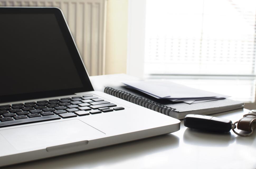 Free Image of Laptop, notebook, envelopes, and car key on office desk near window. 