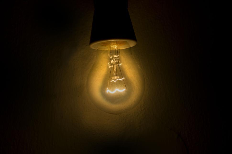 Free Image of Illuminated light bulb glowing warmly in a dark environment. 
