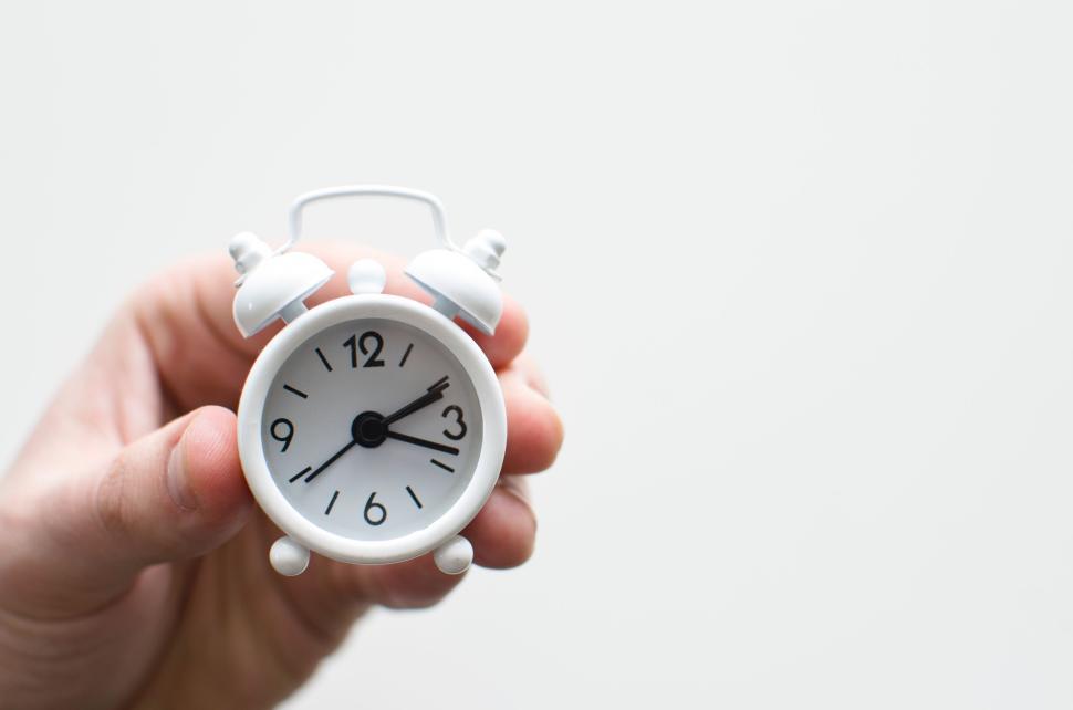 Free Image of Tiny white alarm clock being held in human hands close-up view. 