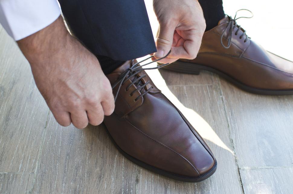 Free Image of Individual tying up brown formal shoes, focusing on hands and laces. 