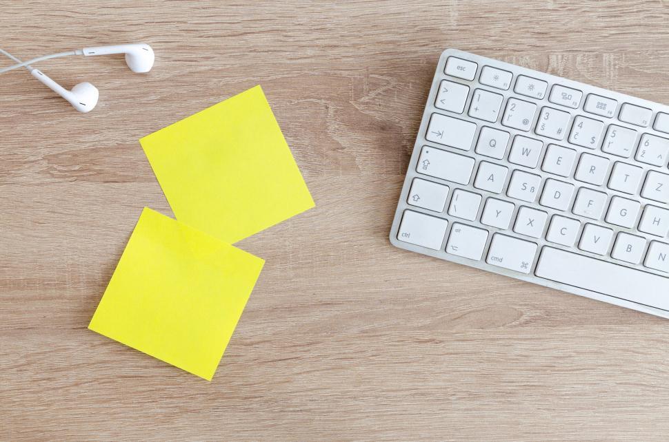 Free Image of Work desk surface with keyboard, earphones, and sticky notes. 
