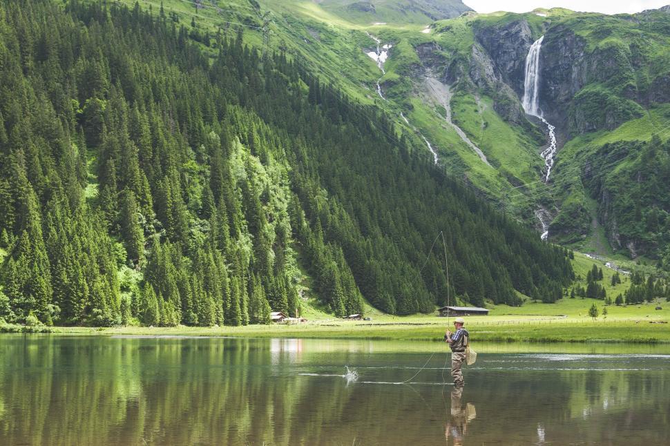 Free Image of A fisherman casts his line in peaceful lake amidst lush mountains 