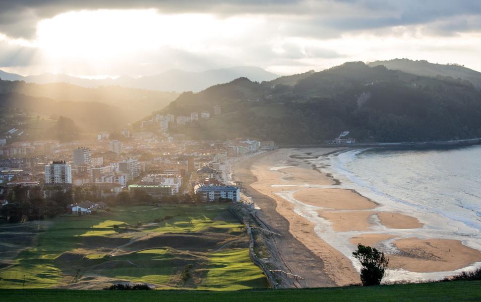 Free Image of Scenic coastal town with beach and mountains during a sunny evening 