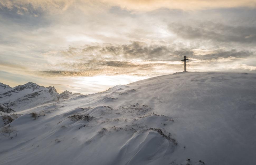 Free Image of Snow-covered mountain peak with a cross standing tall at sunrise 